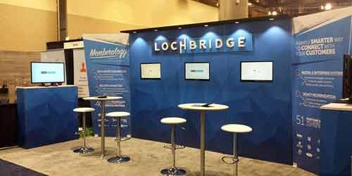 Blue and white example exhibit booth with two tables with stools set up for meetings or demos