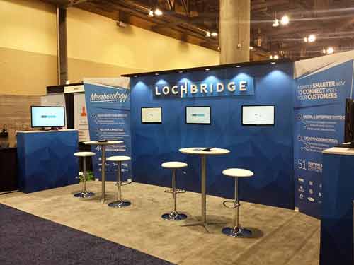 Blue and white example exhibit booth with two tables with stools set up for meetings or demos
